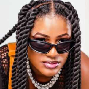 Close-up portrait of a fashionable woman with sunglasses and twisted hairstyles, exuding confidence.