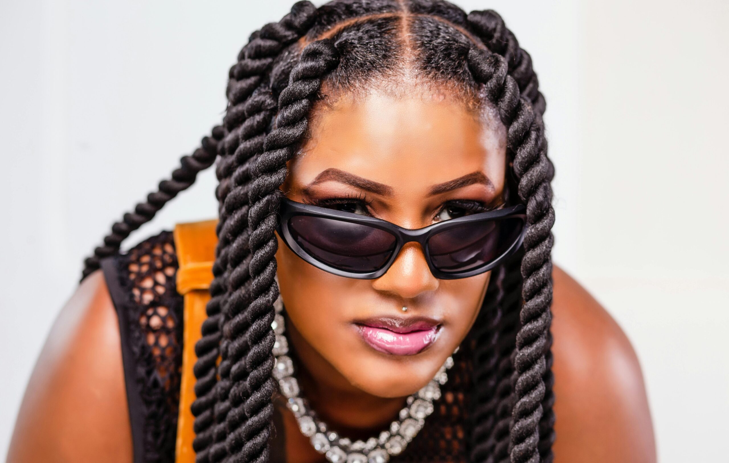 Close-up portrait of a fashionable woman with sunglasses and twisted hairstyles, exuding confidence.